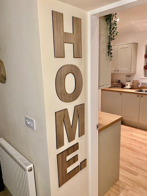 Large letters in an Arial font laser cut and attached to a wall in a vertical style.